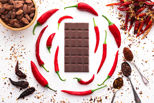 Темний шоколадний батончик, червоний гострий перець чилі кайенн, сухі спеції чилі, порошок какао-бобів, смачний дизайн їжі на чорному дерев'яному фоні - Фото, зображення