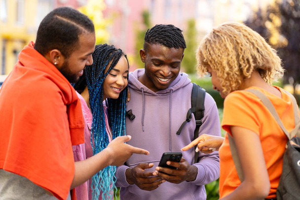 Amici afroamericani sorridenti che tengono smartphone utilizzando l'app mobile per lo shopping online per strada. Tecnologia, internet, concetto di social media  - Foto, immagini