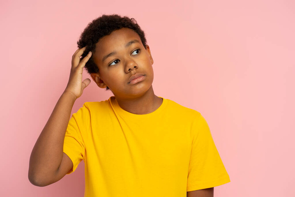 Portrait d'un garçon nigérian sérieux et coûteux portant un t-shirt jaune élégant en pensant au loin isolé sur fond rose, espace de copie - Photo, image
