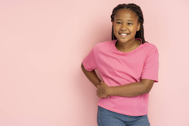 Portrait of cute smiling beautiful African girl with stylish hairstyle in casual clothes posing isolated on pink background, copy space. Pretty fashion female child. Childhood concept - 写真・画像