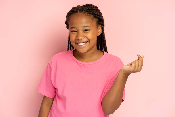 Портрет улыбающейся афроамериканки в розовой футболке, показывающий сердце от пальцев, k поп-культуру, изолированную на розовом фоне, макет. Молодой современный ребенок с зубастой улыбкой смотрит в камеру - Фото, изображение