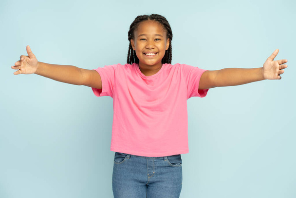 Portrait of positive smiling beautiful African American girl with stylish pigtails wearing casual clothes hugging looking at camera isolated on blue background - Photo, image