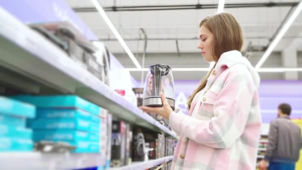 Kadın süpermarketten elektrikli su ısıtıcısı alıyor, kadın müşteri portresi ev aletleri mağazasının koridorunda görünüyor, bayan çaydanlığı inceliyor ve satın alma konusunda karar veriyor, tüketici davranışı - Video, Çekim