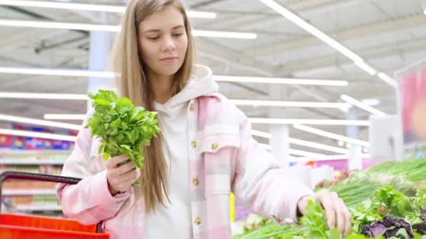 Buyer young blonde woman choosing green leafy vegetables in grocery store. Girl buying greens in supermarket, hypermarket. Parsley, green onion and dill, vegan eco products and healthy food concept. - Footage, Video