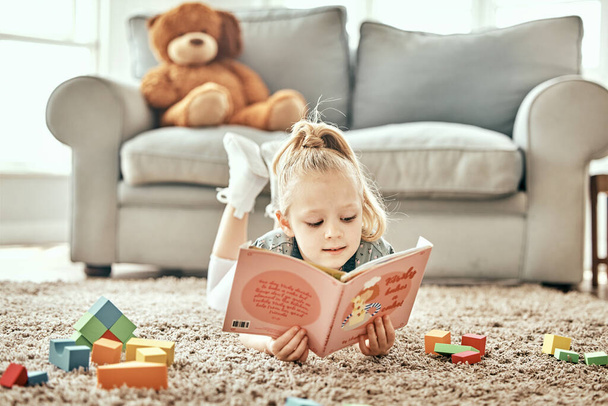 Tanulás, padló és gyermek olvasás egy könyvet az oktatás, fikció vagy tanulás egy otthoni nappaliban. Pihenjen, szőnyeg és egy fiatal lány gyerek egy történet vagy mese egy házban a játék, szórakoztató és kíváncsi. - Fotó, kép