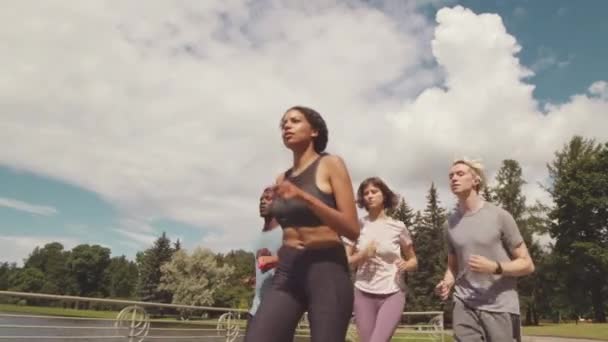 Faible angle moyen slowmo de quatre jeunes athlètes multiraciaux actifs jogging en plein air sur une journée ensoleillée ensemble - Séquence, vidéo