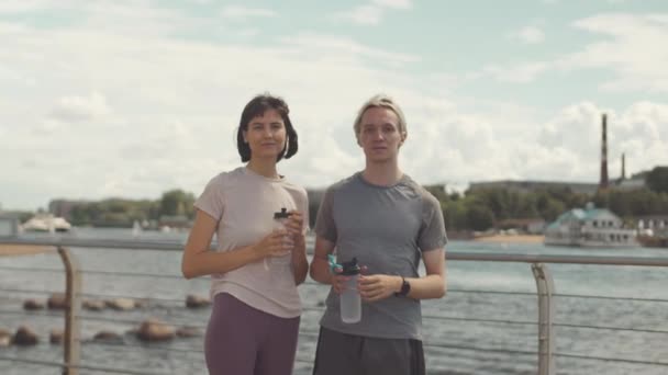 Medium portrait of young sportive Caucasian couple posing for camera standing on city promenade in summer - Footage, Video