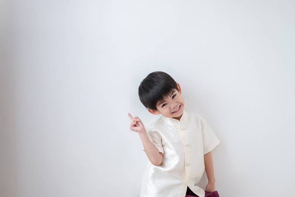 Aasialainen poika yllään perinteisiä thaimaalaisia vaatteita, seisoo etusormi ylöspäin. valkoisella pohjalla - Valokuva, kuva