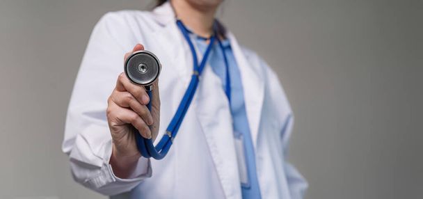 Portret van een vrouwelijke arts met stethoscoop op een platte achtergrond. Gezondheidsconcept Vrouwelijke arts die apparatuur gebruikt om de gezondheid van patiënten te controleren. - Foto, afbeelding