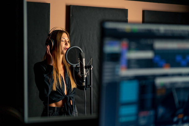 cantora cantando em um estúdio de gravação com fones de ouvido na frente de um microfone para criar uma nova música - Foto, Imagem