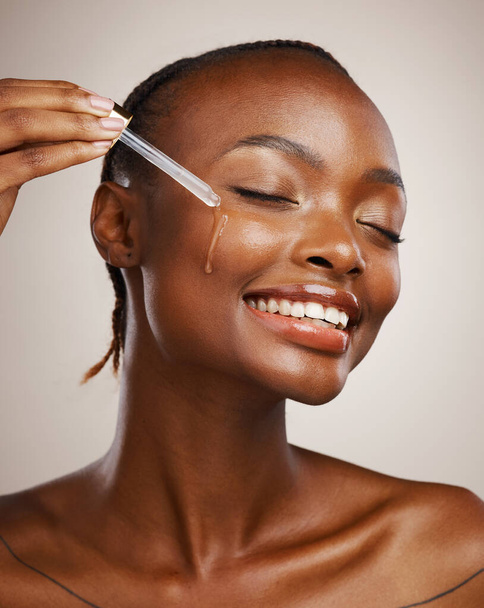 Skincare, woman and smile with dropper on studio background for wellness in cosmetics, beauty or serum. African, person or model by happy, face or relaxed for facial treatment for anti aging oil. - Φωτογραφία, εικόνα