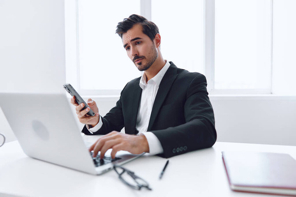 Чоловік дивиться мобільний комп'ютерний дзвінок успішний молодий бізнес-підприємець робоче місце ноутбук офіс сидить зв'язок телефон корпоративний смартфон працівник злий бізнесмен технології - Фото, зображення