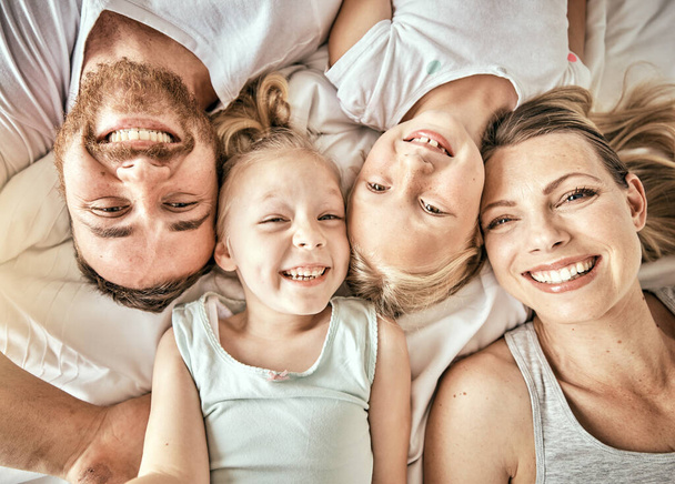 Счастливый, улыбчивый и портрет семьи на кровати для объединения и отдыха вместе в современном доме. Счастье, любовь и вид сверху на девочек, лежащих с родителями из Австралии в спальне дома - Фото, изображение
