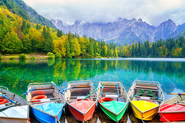 Unterer See Laghi di Fusine, Tarvisio, Italien. Erstaunliche Herbstlandschaft mit Ausflugsbooten im Wasser und farbigem Wald umgeben von Mangart-Gebirge, Outdoor-Reisehintergrund - Foto, Bild
