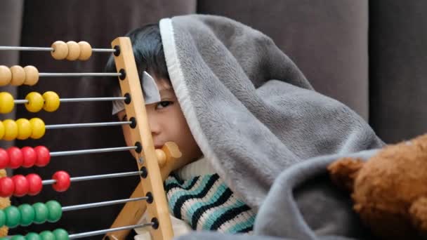  Aziatisch jongen liggend ziek, hij had een koorts verminderen patch op zijn voorhoofd en bedekte zichzelf met een deken als gevolg van de kou. - Video