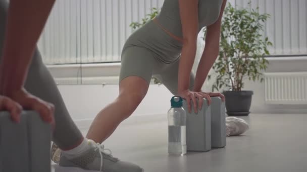 Inclinazione di giovane donna caucasica flessibile in activewear stretto utilizzando blocchi elastici durante lo stretching per le spaccature durante l'allenamento in studio spazioso - Filmati, video