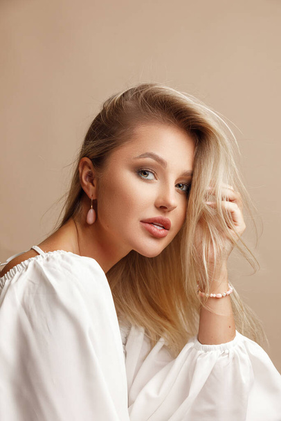 Beautiful young blonde girl wearing exquisite jewelry. Beige background. Pearls, diamonds and gold. - Fotografie, Obrázek