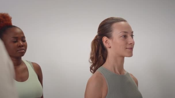 Dwie młode wielonarodowe kobiety trenujące ramię z hantlami w jaskrawo nowoczesnym studiu fitness - Materiał filmowy, wideo