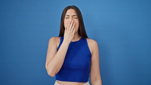 Fiatal gyönyörű spanyol nő nyújtózkodó karok ásít át elszigetelt kék háttér - Felvétel, videó