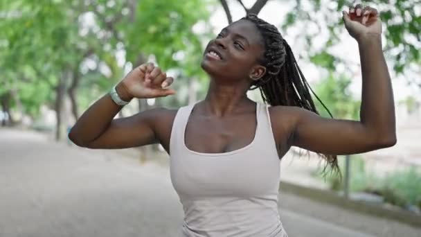 Afrykańska amerykanka uśmiecha się pewnie tańcząc w parku - Materiał filmowy, wideo