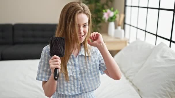 Mujer rubia joven cantando canción usando cepillo como micrófono en el dormitorio - Imágenes, Vídeo