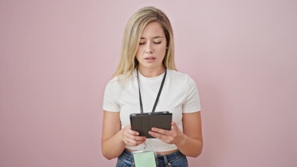 jonge blonde vrouw glimlachen zelfverzekerd met behulp van touchpad over geïsoleerde roze achtergrond - Video
