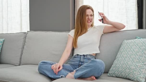 Mujer rubia joven hablando en el teléfono inteligente sentado en el sofá discutiendo en casa - Imágenes, Vídeo