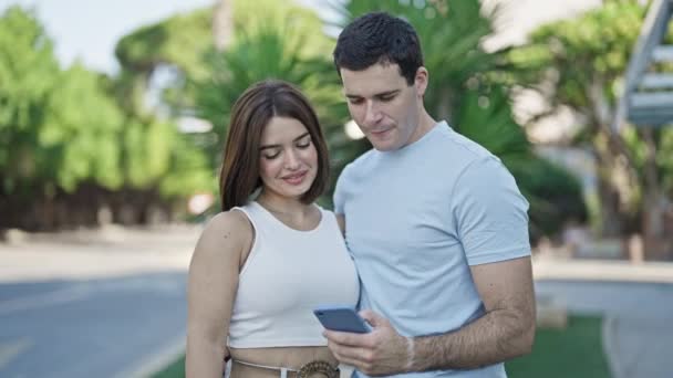 Hermosa pareja sonriendo confiado hacer selfie por teléfono inteligente en el parque - Metraje, vídeo