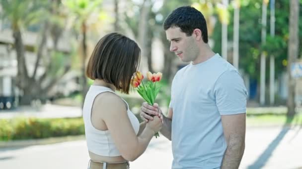 Gyönyörű pár meglepetés csokor virágokkal ölelkezve csókolóznak a parkban. - Felvétel, videó