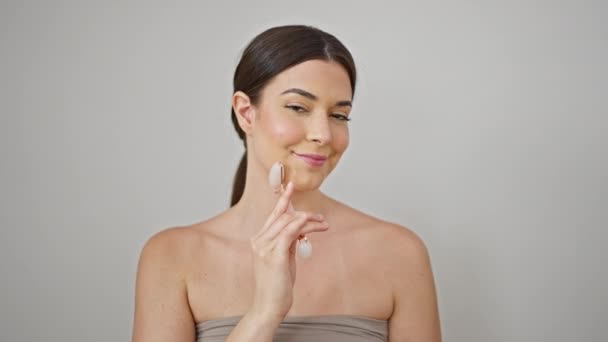 Jovem bela mulher hispânica sorrindo rosto de massagem confiante usando ginásio de pele sobre fundo branco isolado - Filmagem, Vídeo