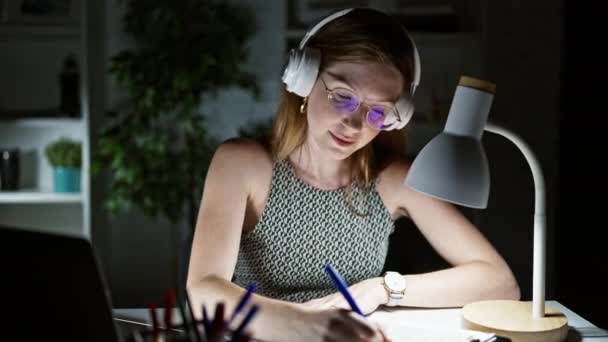 若い金髪女性ビジネスワーカーはオフィスでメモを取る音楽を聞いています - 映像、動画