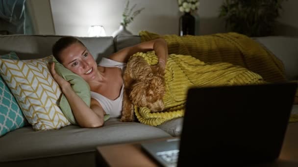 Dizüstü bilgisayarında film izleyen beyaz bir kadın. Evdeki kanepede yatıp gülümsüyor. - Video, Çekim