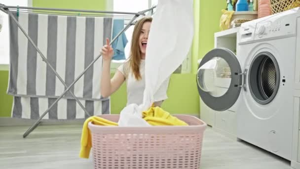 Młoda blondynka rzuca ubrania w powietrze w pralni - Materiał filmowy, wideo