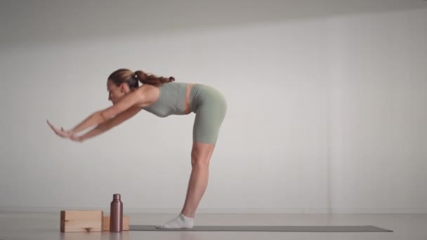 Apuñalada de cuerpo entero de joven mujer caucásica flexible en ropa deportiva ajustada practicando yoga asanas en estera en estudio minimalista brillante - Imágenes, Vídeo