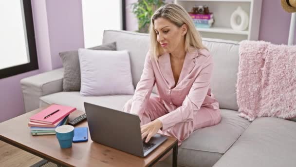Young blonde woman having video call sitting on sofa smiling at home - Footage, Video