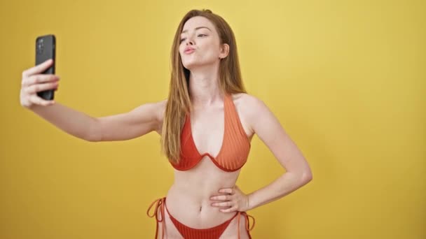 Jeune femme blonde touriste portant un bikini faire selfie par smartphone sur fond jaune isolé - Séquence, vidéo