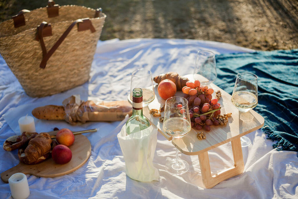 Beautiful cozy autumn picnic by the lake with fruits, pastries and wine. Sun rays. - Photo, Image