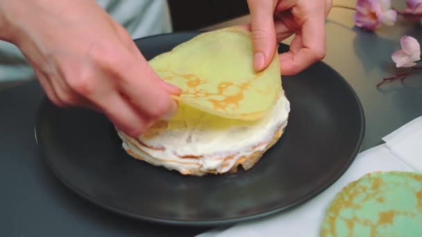 Frauenhände legen einen Pfannkuchen auf eine Creme. Mittlerer Schuss vom Tisch. Kochen in der Küche - Filmmaterial, Video