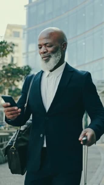 Business man, luggage and phone in city for professional communication, transport and travel news or information. Happy African boss on mobile chat, suitcase and walking outdoor to airport or hotel. - Footage, Video