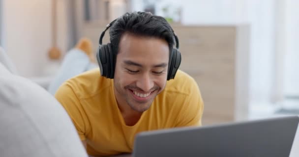 Ακουστικά, laptop και νεαρός άνδρας σε έναν καναπέ βλέποντας μια αστεία, κωμική ή κωμική ταινία στο σαλόνι. Happy, γέλιο και ινδική αρσενικό πρόσωπο streaming μια ταινία ή να δείξει στον υπολογιστή στο σαλόνι στο σπίτι - Πλάνα, βίντεο
