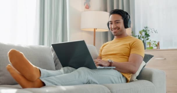 Mies, kannettava tietokone ja kuulokkeet sohvalla musiikkia, e-oppiminen ja rentoutua online-koulutuksen ja onnellinen tilaus kotona. Nuori aasialainen opiskelija audio streaming, kirjoittamalla tietokoneella ja laulaa kpop. - Materiaali, video