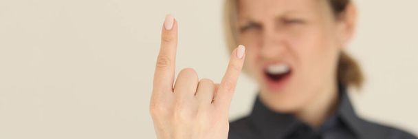 Woman with open mouth shows horns gesture with index and little fingers standing on beige background. Blurry female person does rock star sign closeup - Photo, Image