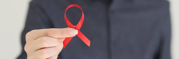 Γυναίκα κατέχει κόκκινη κορδέλα που αντιπροσωπεύει την καταπολέμηση του AIDS. Σύμβολο ευαισθητοποίησης και αλληλεγγύης με τους οροθετικούς ανθρώπους και τα άτομα που ζουν με AIDS - Φωτογραφία, εικόνα