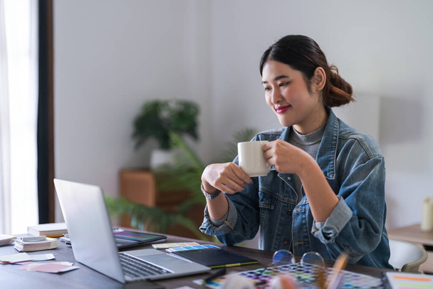 A grafikus tervező nők kávét isznak, és adatokat olvasnak a laptopon gondolkodás logó márka grafikai tervezés. - Fotó, kép