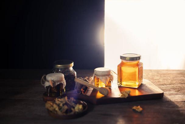 miel natural Ecológico envasado en botellas de vidrio Colocado en una mesa de madera, fondo negro oscuro. - Foto, imagen