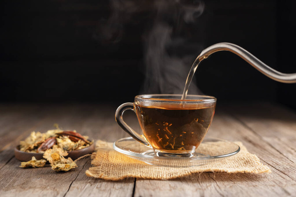 Udělejte si šálek horkého čaje nebo sklenici chryzantémového čaje. a chryzantémy ležely na dřevěném stole Nalévání zdravých nápojů, bylinných nápojů a lékařské koncepce - Fotografie, Obrázek