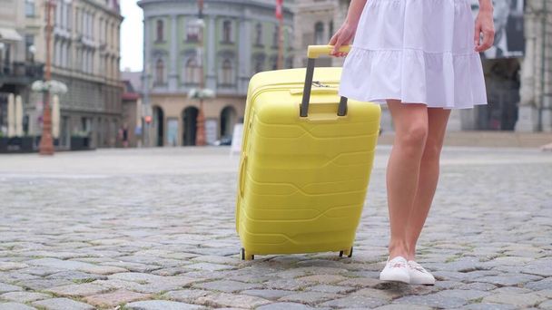 Close-up of a female traveler in a Euroaean city carrying her yellow bag on a cart. Summer vacation. A tourist in the city. - Photo, Image