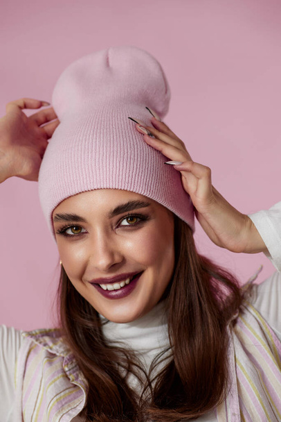 portrait of happy playful woman keeps hands on pink hat on pastel pink background. - Foto, imagen