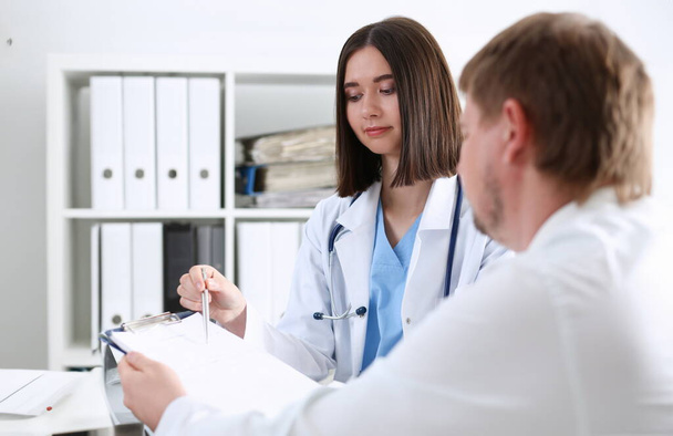 Beautiful smiling female doctor hold silver pen filling patient history list at clipboard pad. Physical exam er disease prevention ward round 911 prescribe remedy healthy lifestyle concept - Photo, Image