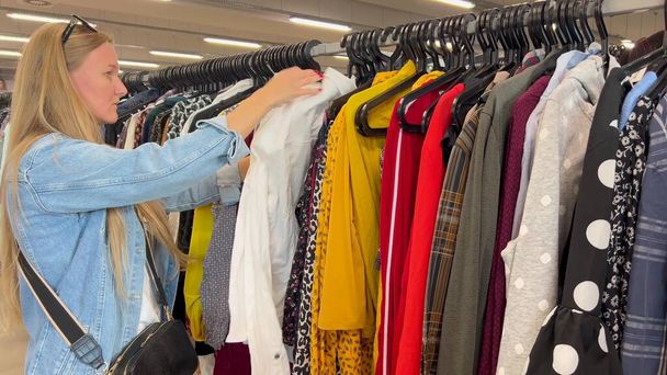Een vrouw onderzoekt kleren in een vrouwenwinkel. Winkelen voor kleding tegen kortingen. zwarte vrijdag. - Foto, afbeelding